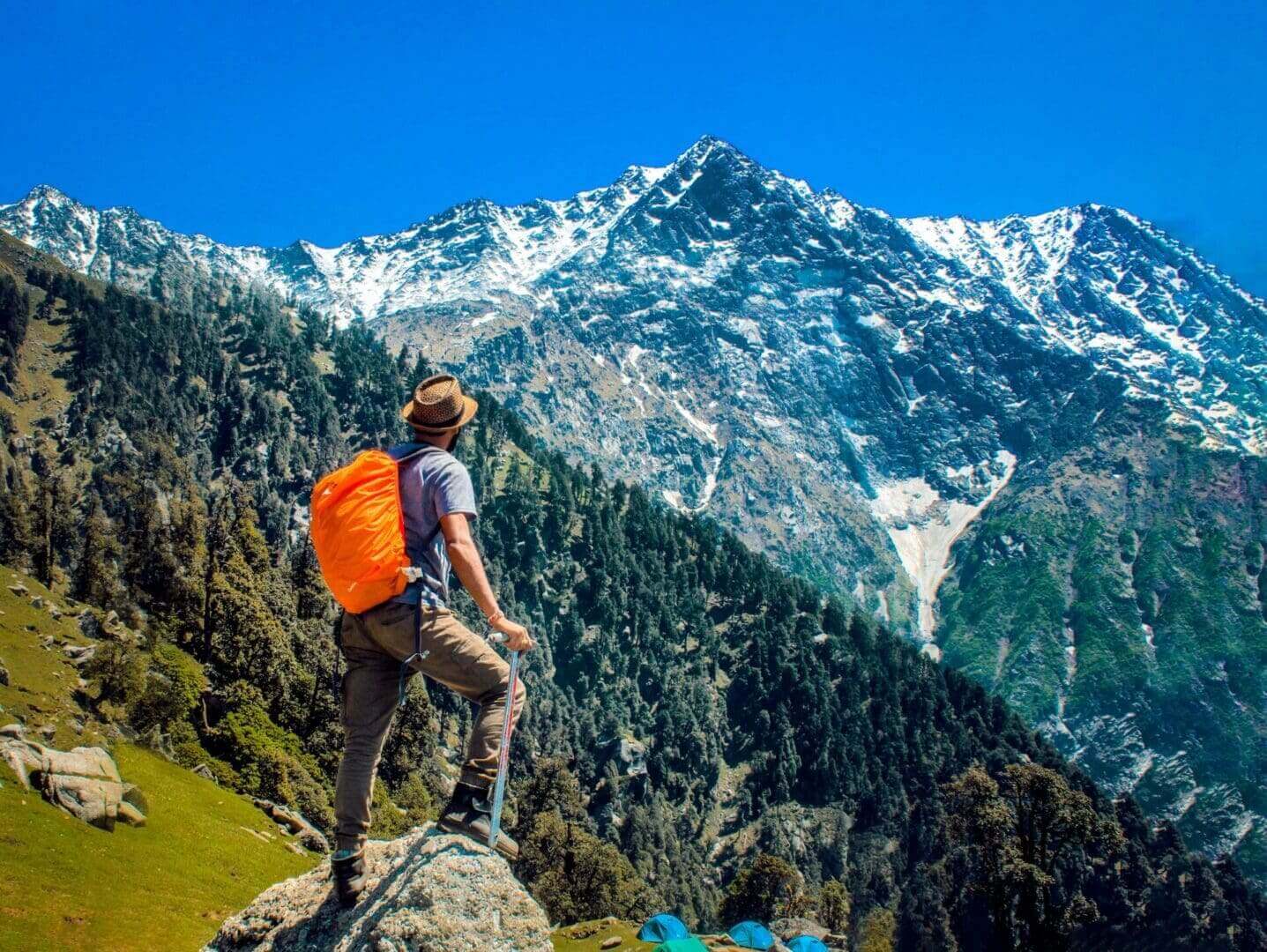 A man with an orange backpack standing on top of a rock.